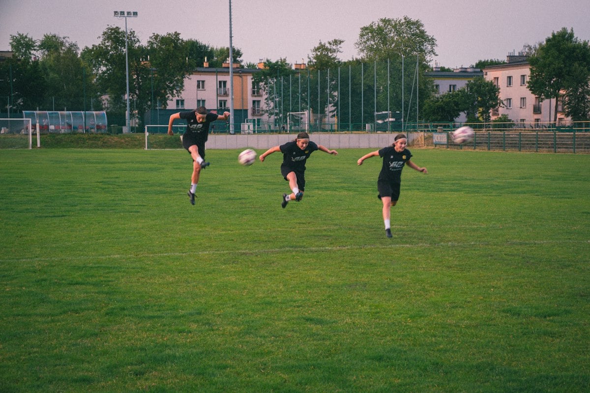 Three soccer players airborne on a green field during the kind of explosive jumping used in plyometric training
