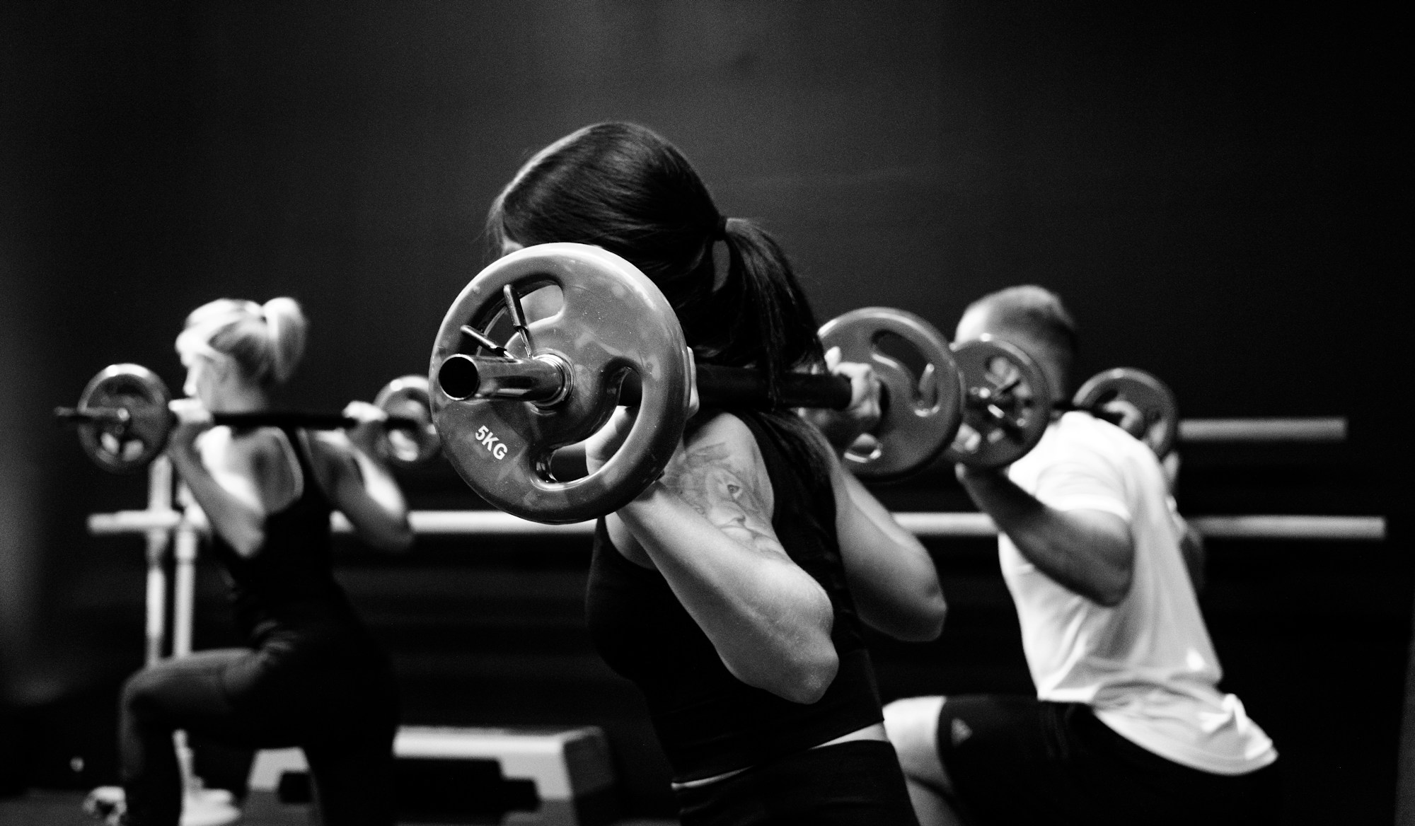 Three people lifting barbells in a gym, where rest intervals between sets shape session length