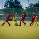 Footballers running on a sunlit pitch, the outdoor setting where heat stress lowers intermittent fitness test scores