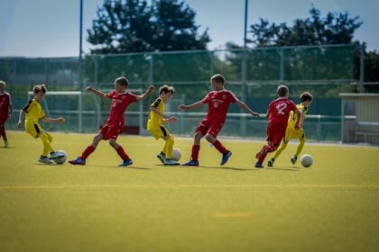 Footballers running on a sunlit pitch, the outdoor setting where heat stress lowers intermittent fitness test scores