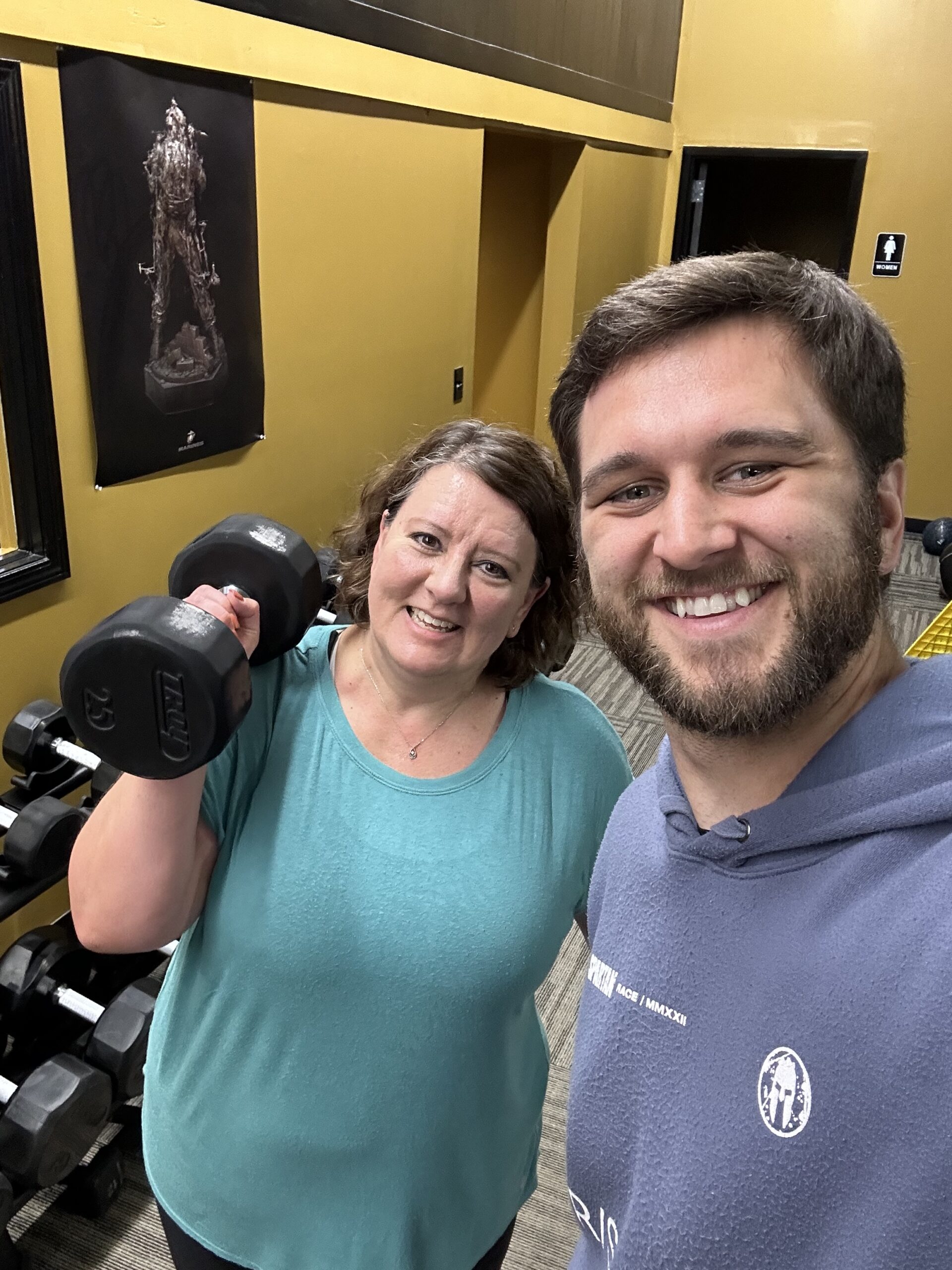 Two people smiling beside dumbbells at G Fitness