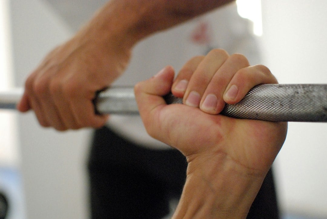 Hands gripping a loaded barbell between repetitions, the short pauses that define cluster training