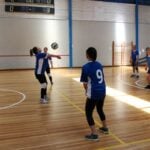 Students playing volleyball in a university sports session on an indoor wooden court