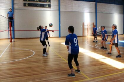 Students playing volleyball in a university sports session on an indoor wooden court