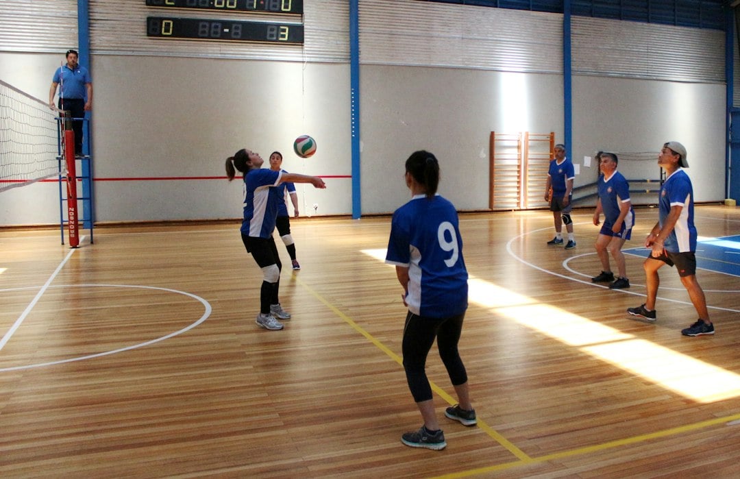 Students playing volleyball in a university sports session on an indoor wooden court