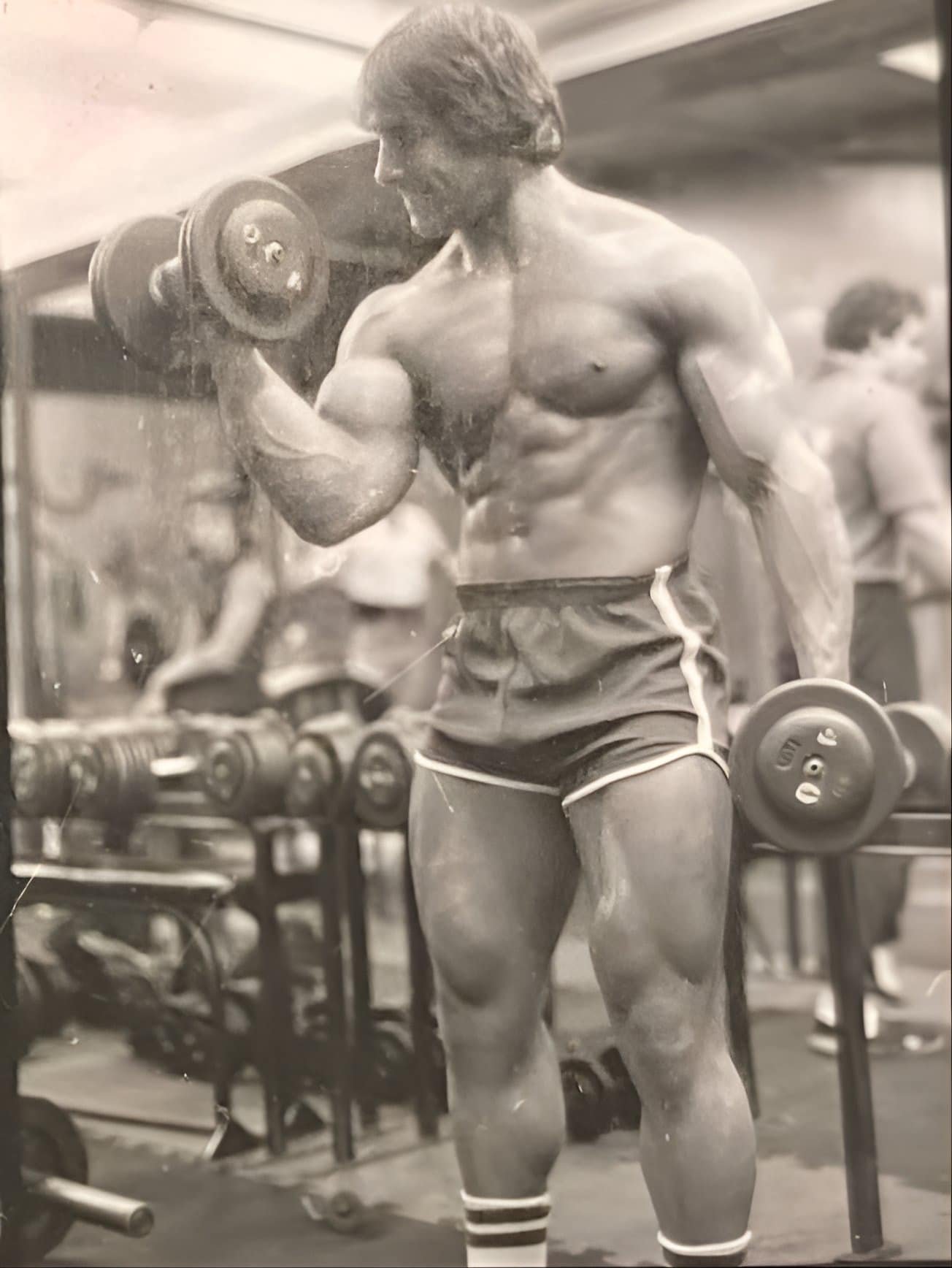 John DeFendis performing a dumbbell curl in an archival gym photograph