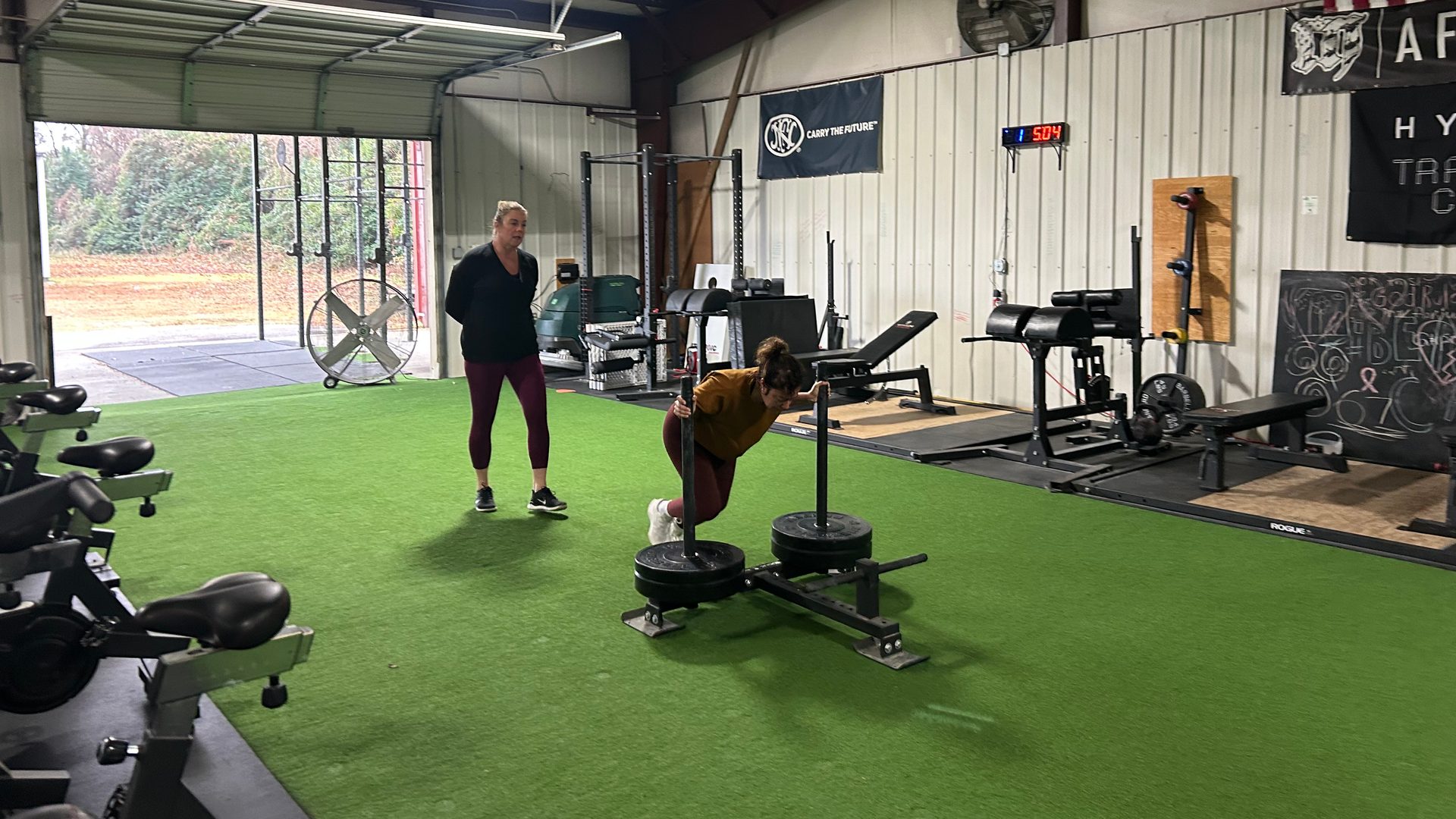 A coach watches a member push a loaded sled at Lodestar Fitness