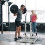 Man performing a barbell squat with a coach in a gym