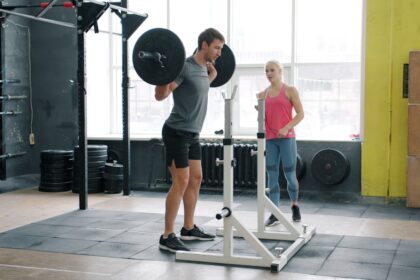 Man performing a barbell squat with a coach in a gym