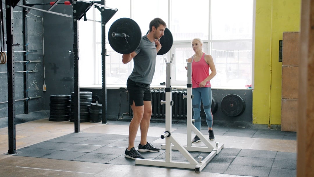 Man performing a barbell squat with a coach in a gym