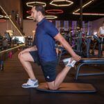 Athlete performing a lower-body strength exercise with a trainer, illustrating quadriceps and joint positioning