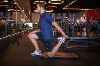 Athlete performing a lower-body strength exercise with a trainer, illustrating quadriceps and joint positioning