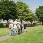 Adults walking together along a sunny park path, the kind of weekly activity studied for Parkinson disease progression